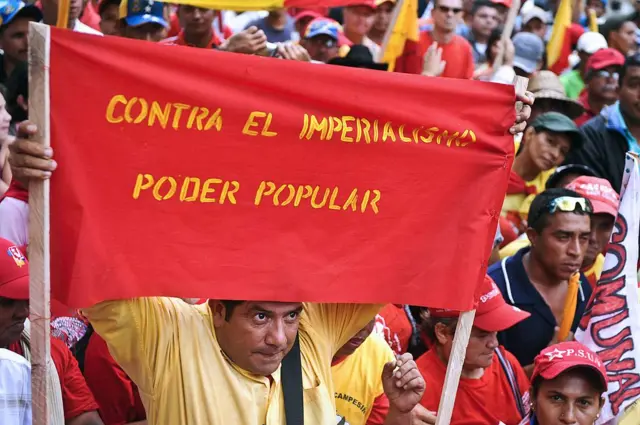 Un hombre carga una pancarta roja con un mensaje que dice: "Contra el imperialismo, poder popular".