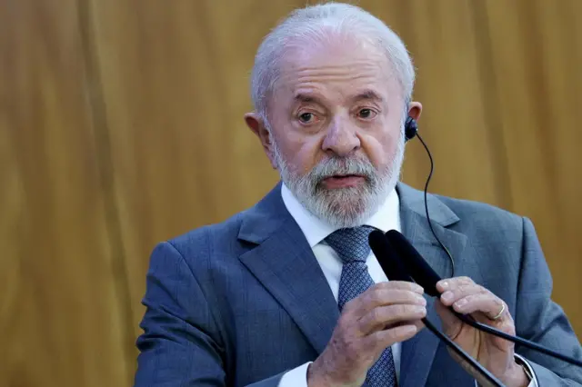 Lula olhando compenetrado para algo, usando fone para tradução e mexendo em microfone