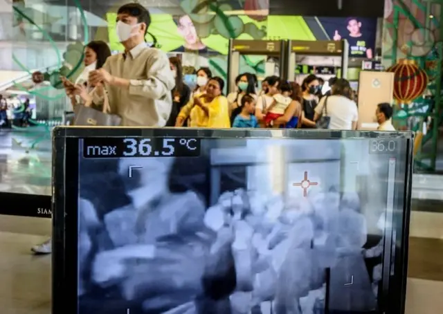 People with protective face masks pass in front of a thermal scanner as they enter a shopping mall in Bangkok on January 29, 2020.
