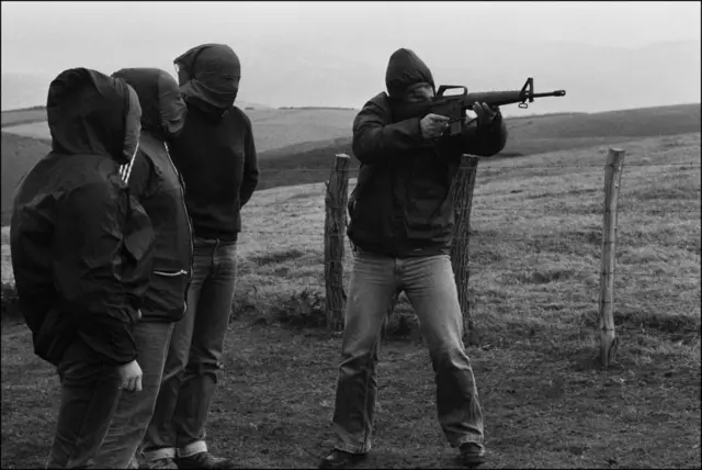 Un encapuchado de ETA sujeta y apunta con un fusil durante un entrenamiento mientras otros tres militantes encapuchados le observan en una imagen de 1978.  