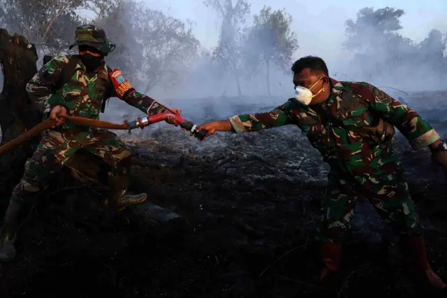 Personel Koramil 1207-05/Sungai Raya saling menyerahkan nozel selang pemadam kepada rekannya saat mengakhiri penyemprotan karena pasokan air habis di lahan karhutla di belakang Komplek Arwana Indah, Desa Limbung, Kecamatan Sungai Raya, Kabupaten Kubu Raya, Kalimantan Barat, Selasa (4/8/2026). Pemadaman yang dilakukan tim gabungan BPBD Kabupaten Kubu Raya, TNI/Polri, Manggala Agni, relawan damkar swasta, dan instansi terkait tersebut merupakan upaya mencegah api meluas ke kawasan sekitar, termasuk permukiman dan Bandara Supadio yang berjarak sekitar dua kilometer dari lokasi karhutla. 