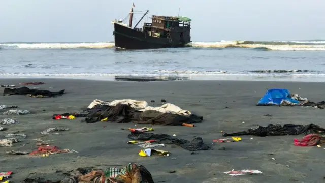 Belongings of Rohingya refugees scattered on the shore as their carrier boat is seen in the background