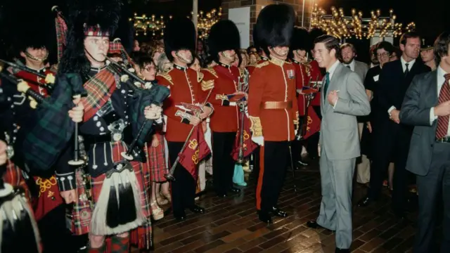 Принц у сивом оделу окружен групом људи у црвеним униформама Краљеве гарде