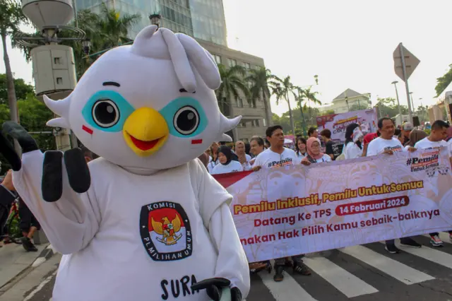 Peserta dan maskot Pemilu 2024 Sura membawa spanduk informasi pemungutan suara saat kegiatan KPU Goes to Car Free Day (CFD) di Bundaran HI, Jakarta Pusat, Minggu (03/12).