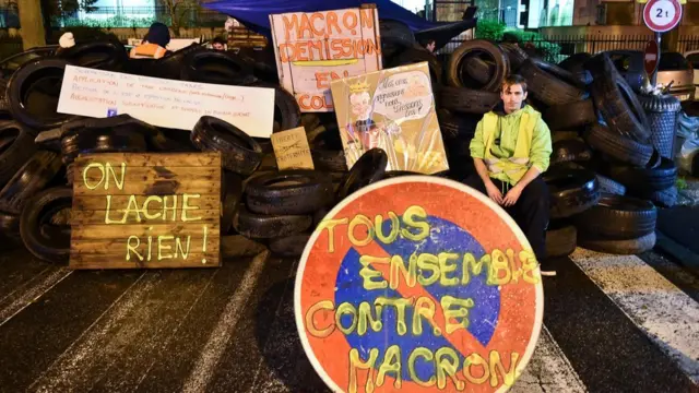 A demonstrator wearing a yellow vest (gilet jaune) sits on a barricade of tires, at the entrance of the Tax Office in Rennes, northwestern France, on December 2, 2018