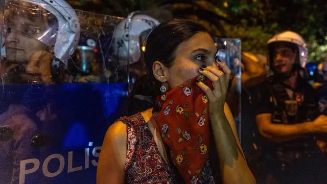 Saraçhane mitingine katılan genç bir kadın, yüzü eşarpla kapalı bir şekilde polis barikatının önünde duruyor.