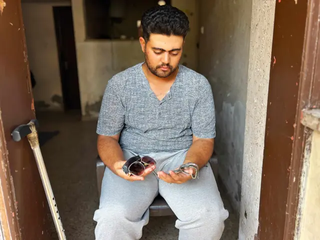 グレーの半袖の服を着た男性が、サングラスや腕時計を乗せた両手を広げている