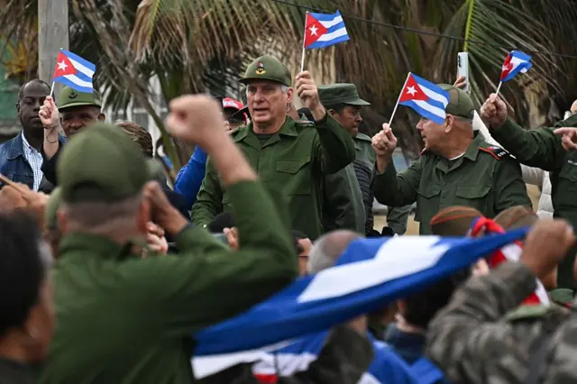 Miguel Díaz-Canel, sosteniendo una bandera cubana vestido con uniforme militar, junto a otros oficiales del ejército