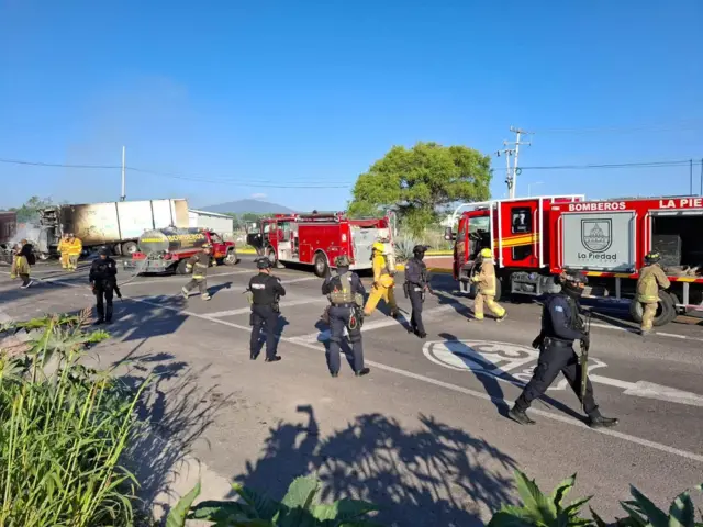 Bomberos y policías en el punto de un bloqueo carretero con vehículos incendiados en Michoacán