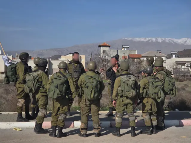 صورة لرجال يرتدون زياً عسكرياً، وتظهر في الخلفية مبان وتلال