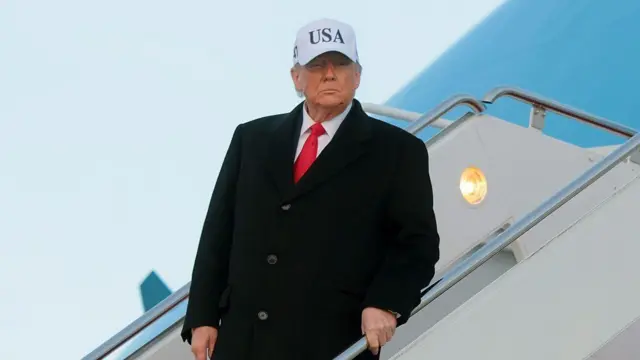 Trump, na escada do avião, usando um boné escrito USA