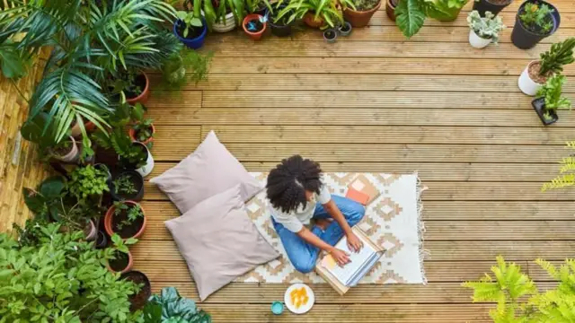 Une femme travaille assise sur un tapis dans son jardin