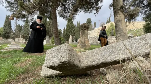 The Greek patriarch stands near desecrated graves at the Mount Zion cemetery in Jerusalem