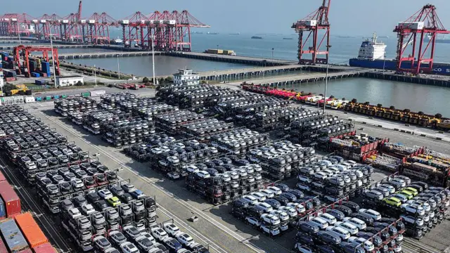 中国東部の江蘇省にある蘇州の港で、積み上げられた自動車が列をなしている。荷揚げドックとクレーンが見え、その向こうには海が広がっている (2025年4月7日)