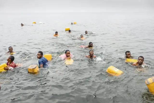 Residents swim while carrying their jerry cans as they gather to collect water.
