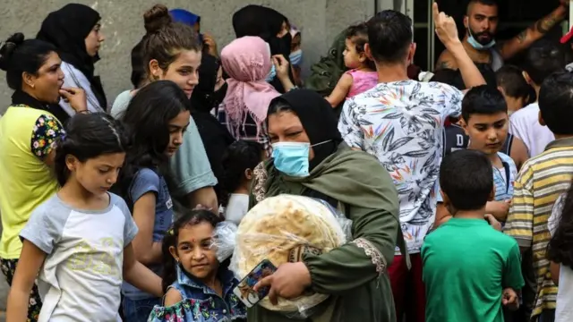 A woman leaves a bakery with a bag of bread as people wait for their turn, in the neighbourhood of Nabaa in the Lebanese capital Beirut's southern suburbs, on August 13, 2021,