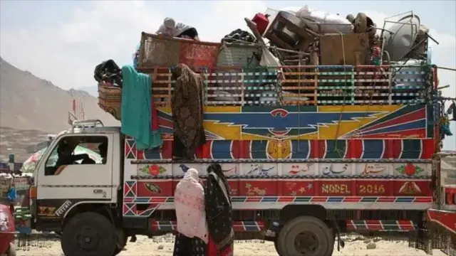 موتری از وسایل مهاجران افغان - دو زن با چادرهای سیاه و سفید در کنار لاری ایستاده‌اند