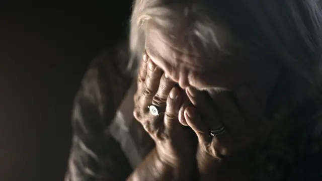 Mulher idosa triste, com as mãoes no rosto