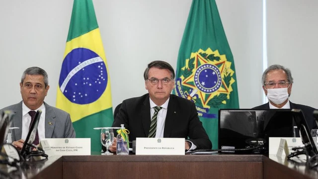 Braga Netto, Bolsonaro e Guedes sentadobc online casinomesabc online casinoreunião, com feições sérias e bandeiras no planobc online casinofundo