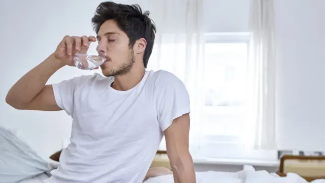 Un hombre bebiendo agua en cama,