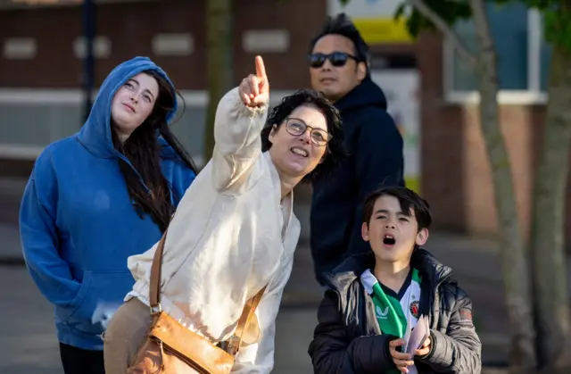 Una mujer apunta al cielo mientras su hijo sostiene una colección de marcapáginas