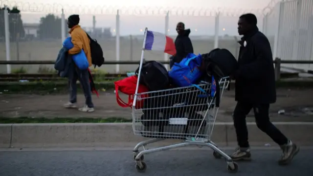 A man pushes a shopping trolley carrying his belongings and a French flag