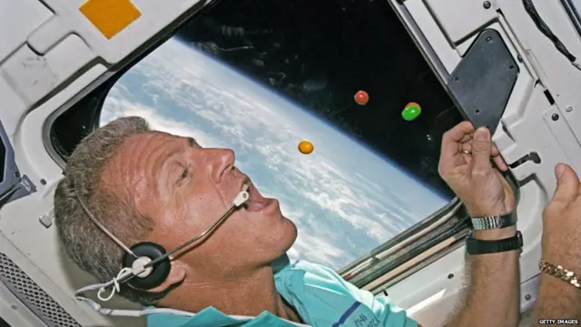 Astronaut Loren Shriver pursues several floating chocolate candies on the flight deck of the Space Shuttle Atlantis in 1992