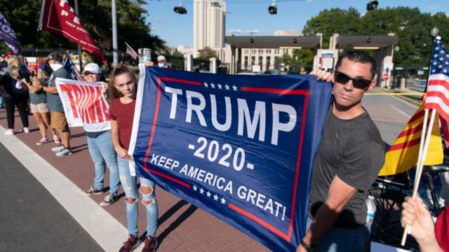 Сторонники Дональда Трампа у здания больницы, где он проходит лечение. На плакате написано: "Трамп - 2020. Сохраним Америку великой"