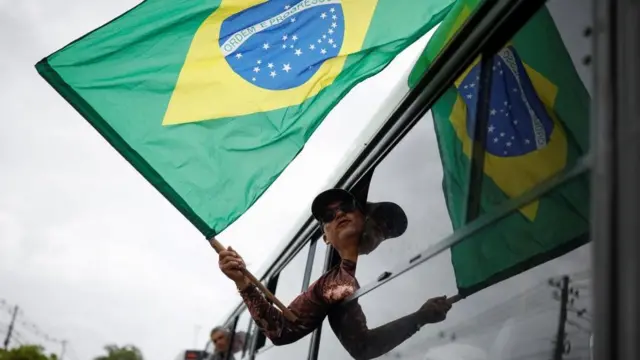 Um homem segura a bandeira do Brasil pela janelacodeshare online for doubledown casinoum ônibus enquanto é detido após a invasãocodeshare online for doubledown casinoBrasília por apoiadorescodeshare online for doubledown casinoBolsonaro