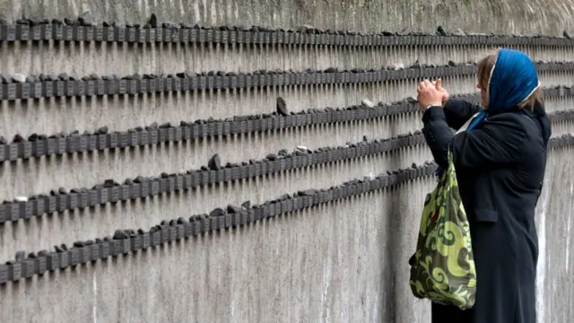 жена пали свећу на меморијалу