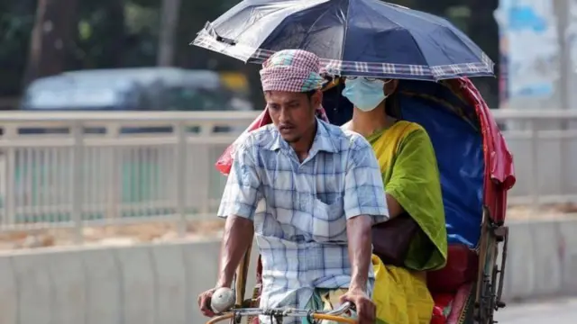 রিকশায় করে ছাতা মাথায় দিয়ে এক নারী যাচ্ছেন 