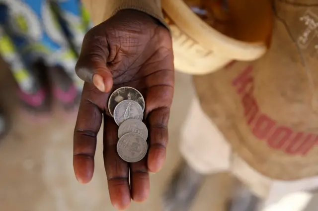 Main tendue d'un talibé tenant des pièces de francs CFA.