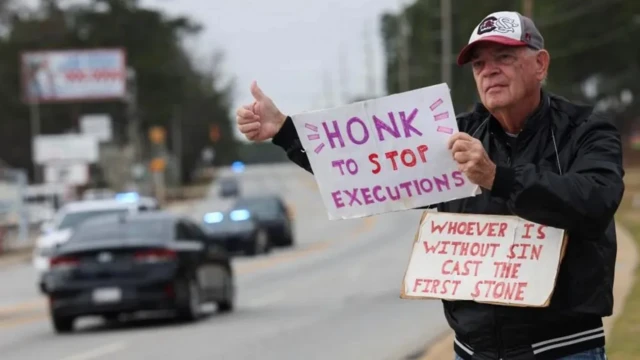 Foto of man wit im thumbs up on di side of di road wey dey tell motorists make dem "honk to stop executions" 