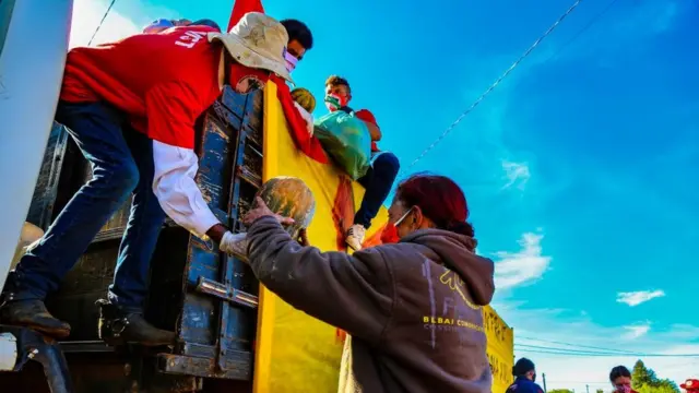 Do altoaposta gratis hojeum caminhão, um integrante do MST entrega uma abóbora para uma mulher, ambos usam máscarasaposta gratis hojeproteção contra a covid