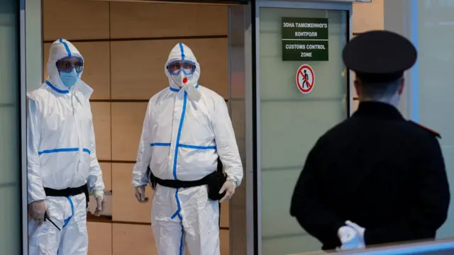 Служащие в защитных костюмах в аэропорту