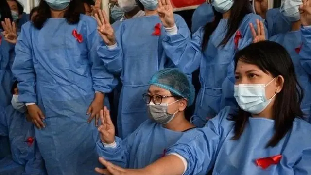 บุคลากรทางการแพทย์โรงพยาบาลย่างกุ้งติดริบบิ้นสีแดงและชูสามนิ้วเพื่อประท้วงการก่อรัฐประหารของกองทัพ