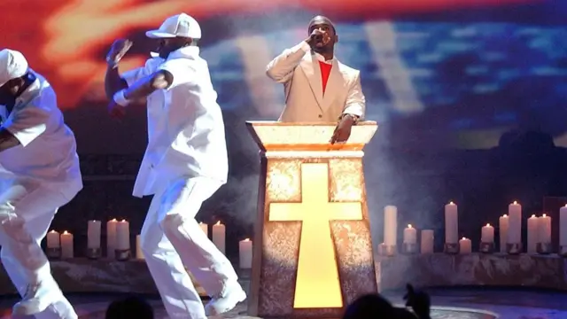 嘻哈歌手坎耶有个绰号是"Yeezus"（与耶稣Jesus谐音）。上图是他在舞台上演绎嘻哈音乐作品《与耶稣同行》（Jesus Walks）时的照片。