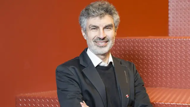 O pesquisador Yoshua Bengio posa sorrindojogo que realmente ganhar dinheiro no pixfrente a um fundo vermelho