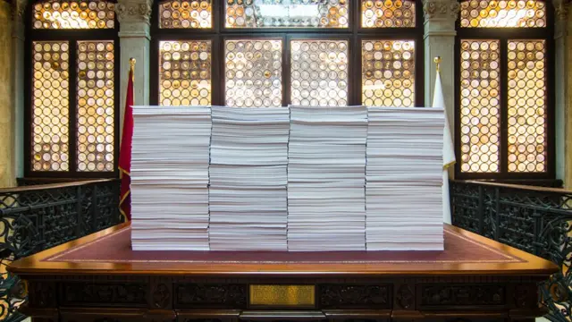 انبوه پرونده ها و ایمیلهای چاپ شده روی یک میز تحریر بزرگ