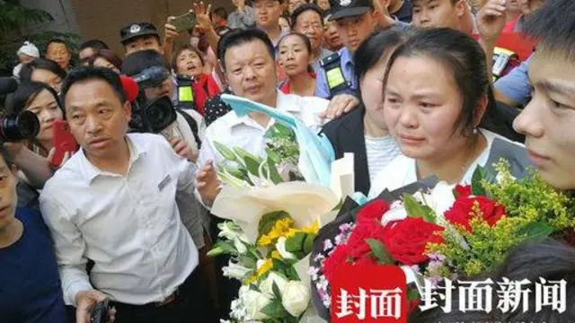 Kang Ying segurando flores, rodeada pela família