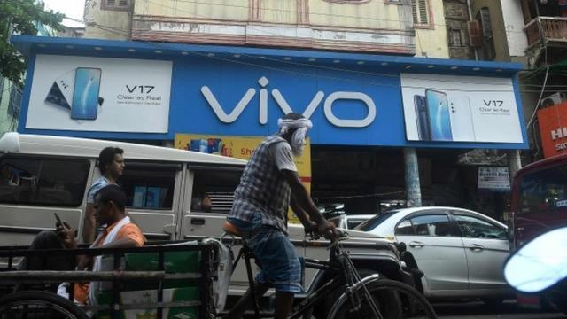Commuters pass by an advertising board of Chinese mobile phone maker VIVO on a street in Kolkata on June 22, 2020