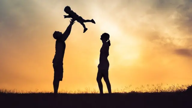 Casal brinca com uma criança pequena ao pôr do sol