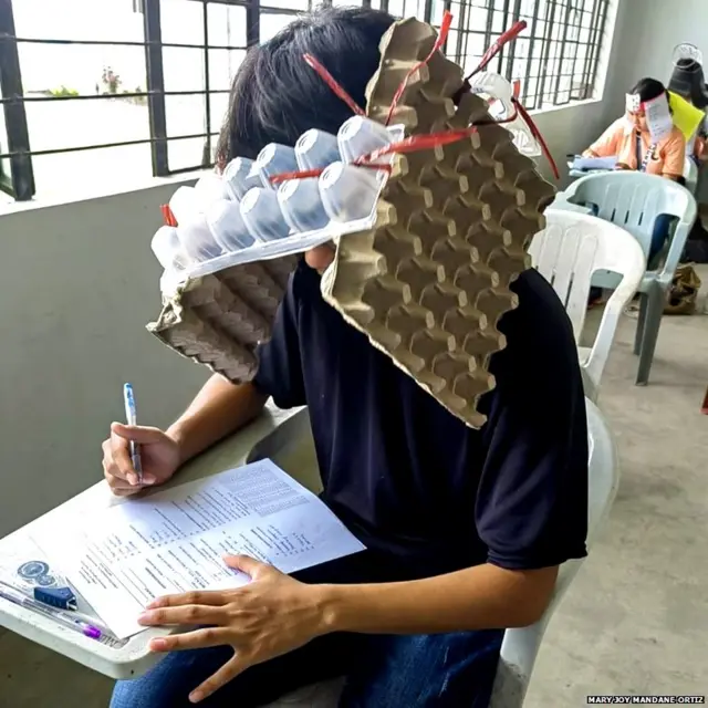 ਫਿਲੀਪੀਨਜ਼ ਵਿੱਚ ਇੱਕ ਕਾਲਜ ਇਮਤਿਹਾਨ ਦੌਰਾਨ ਇੱਕ ਵਿਦਿਆਰਥੀ ਅੰਡੇ ਦੇ ਡੱਬਿਆਂ ਤੋਂ ਬਣੀ ਘਰੇਲੂ ਟੋਪੀ ਪਹਿਨੇ ਹੋਏ