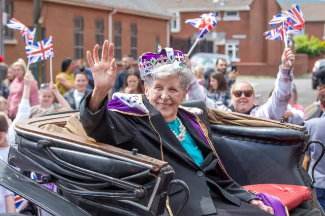 A woman sitting in carriage and wearing a crown waves to the public as she takes part in the celebrations for the Platinum Jubilee on Donegall Pass in Belfast, Northern Ireland, on 3 June 2022