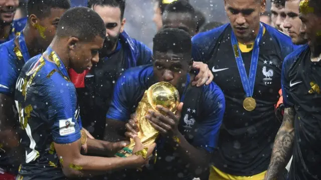 L'attaquant français Kylian Mbappé (G) tient le trophée tandis que le défenseur Samuel Umtiti (C) l'embrasse