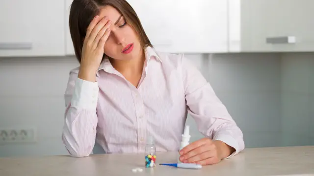 Mujer con dolor de cabeza frente a un frasco de pastillas