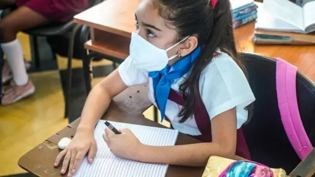 Une élève en masque, devant une table sur laquelle est posé son cahier