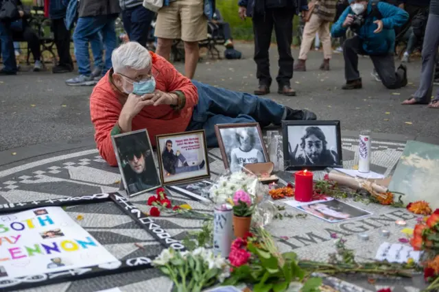 Un hombre se toma un foto frente a unas fotos y recuerdos conmemorativos de la vida de John Lennon en Strawberry Fields, Central Park, Nueva York