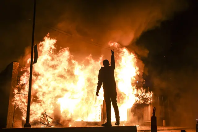 16. A man poses in front of a burning building during unrest resulting from the killing of an unarmed black man, George Floyd, by police