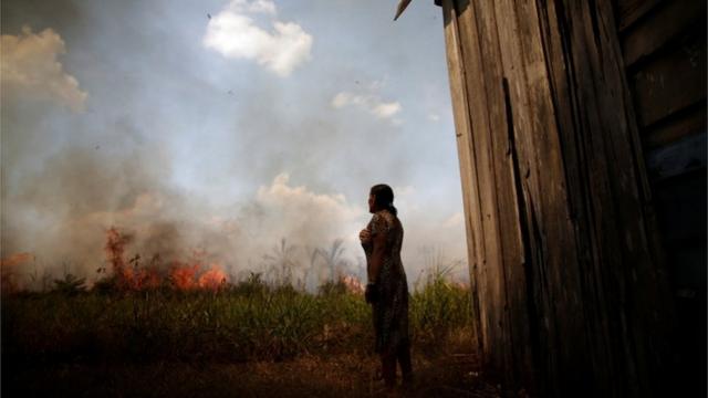 Mulher do lado de fora de casa observando floresta queimando ao fundo